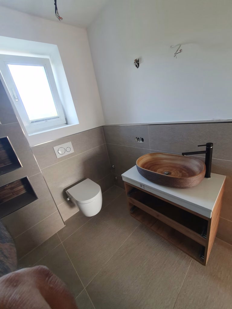 Zidna WC šolja i nadgradni lavabo sa crnom slavinom u popločanom kupatilu na Voždovcu.