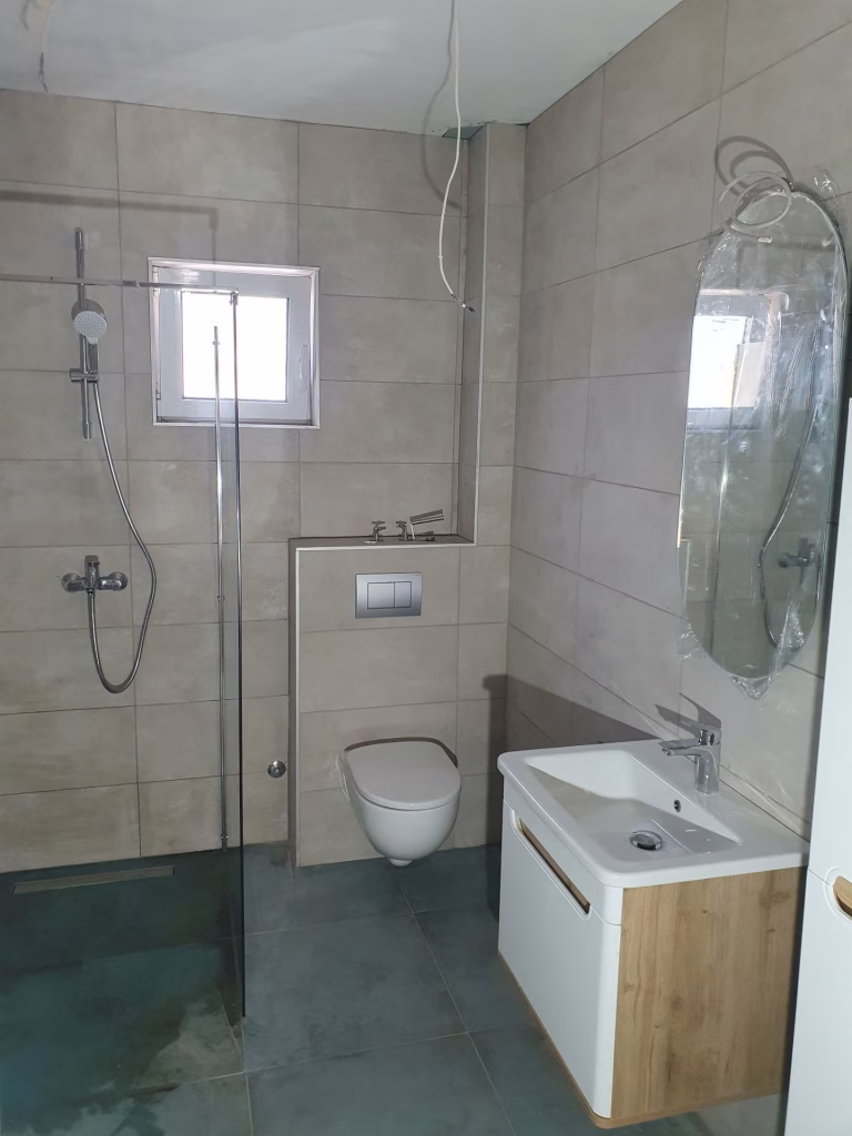 Kupatilo sa staklenom tuš zonom, zidnom WC šoljom i lavabo ormarićem na Voždovcu.